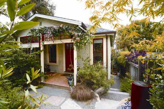 Alma’s Earthquake Cottage is flanked on three sides by her garden, an integral part of the overall style. A spill jar welcomes visitors on the right; small trees, shrubs and vines shape an oasis. An evergreen clematis drapes the front porch, one of many scented plants that bloom at different times of the year.
